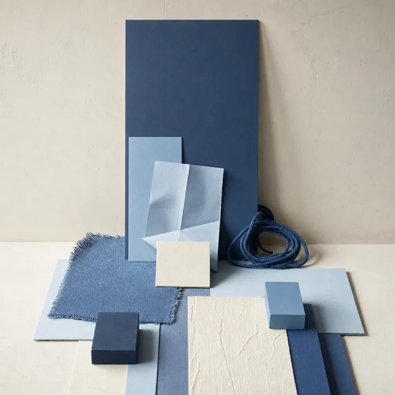 Still life of an upright rectangular sheet of paper like a screen, with folded paper and a coiled cable in front, in shades of blue against a light wall.